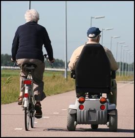 Two men (one riding a bike, the other using a power wheelchair) on a path.